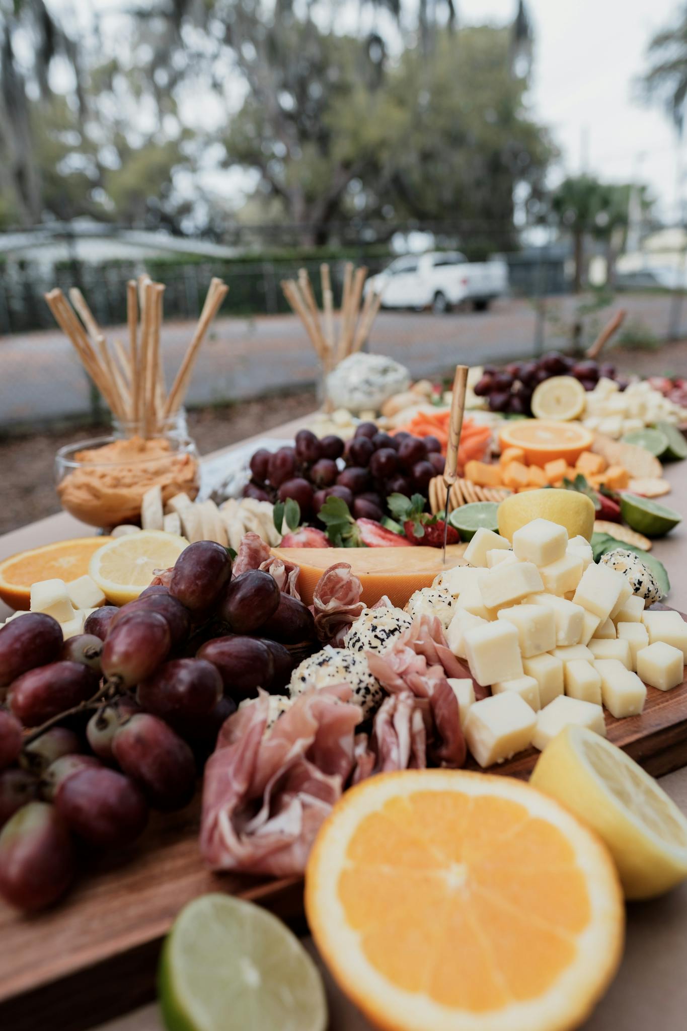 A colorful charcuterie board with cheese, meats, and fruits set up outdoors in a tropical setting.
